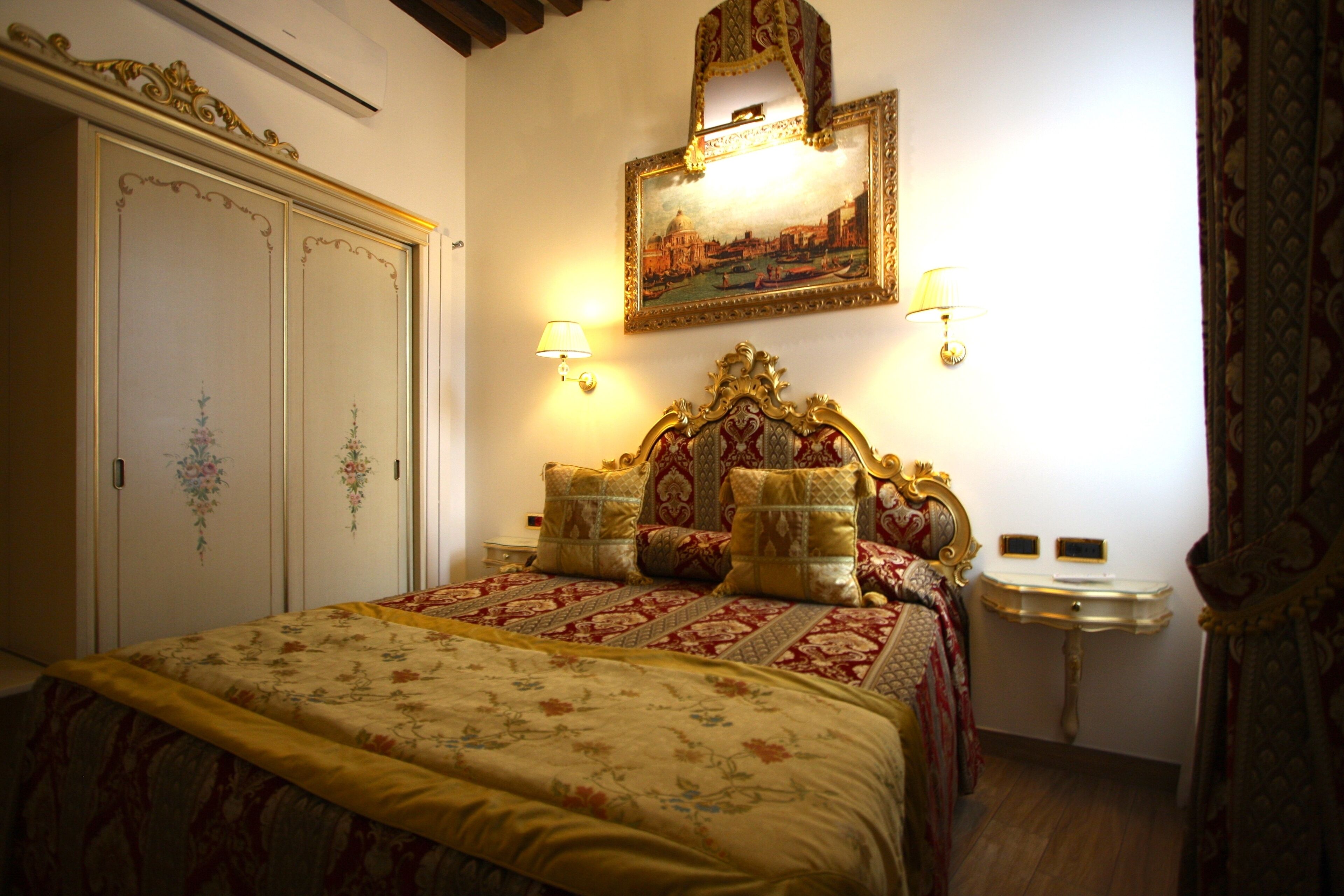 Un dormitorio con una cama grande, cabecera decorada, dos lámparas de pared, un espejo y una mesita de noche pequeña.