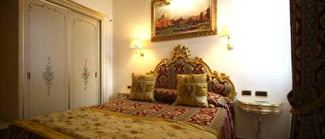 Un dormitorio con una cama grande, cabecera decorada, dos lámparas de pared, un espejo y una mesita de noche pequeña.