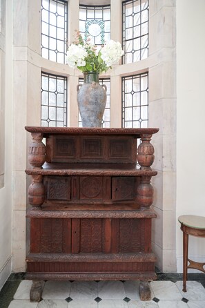 A wooden cabinet with intricate carvings, a vase with white flowers, and a window with a decorative grille.