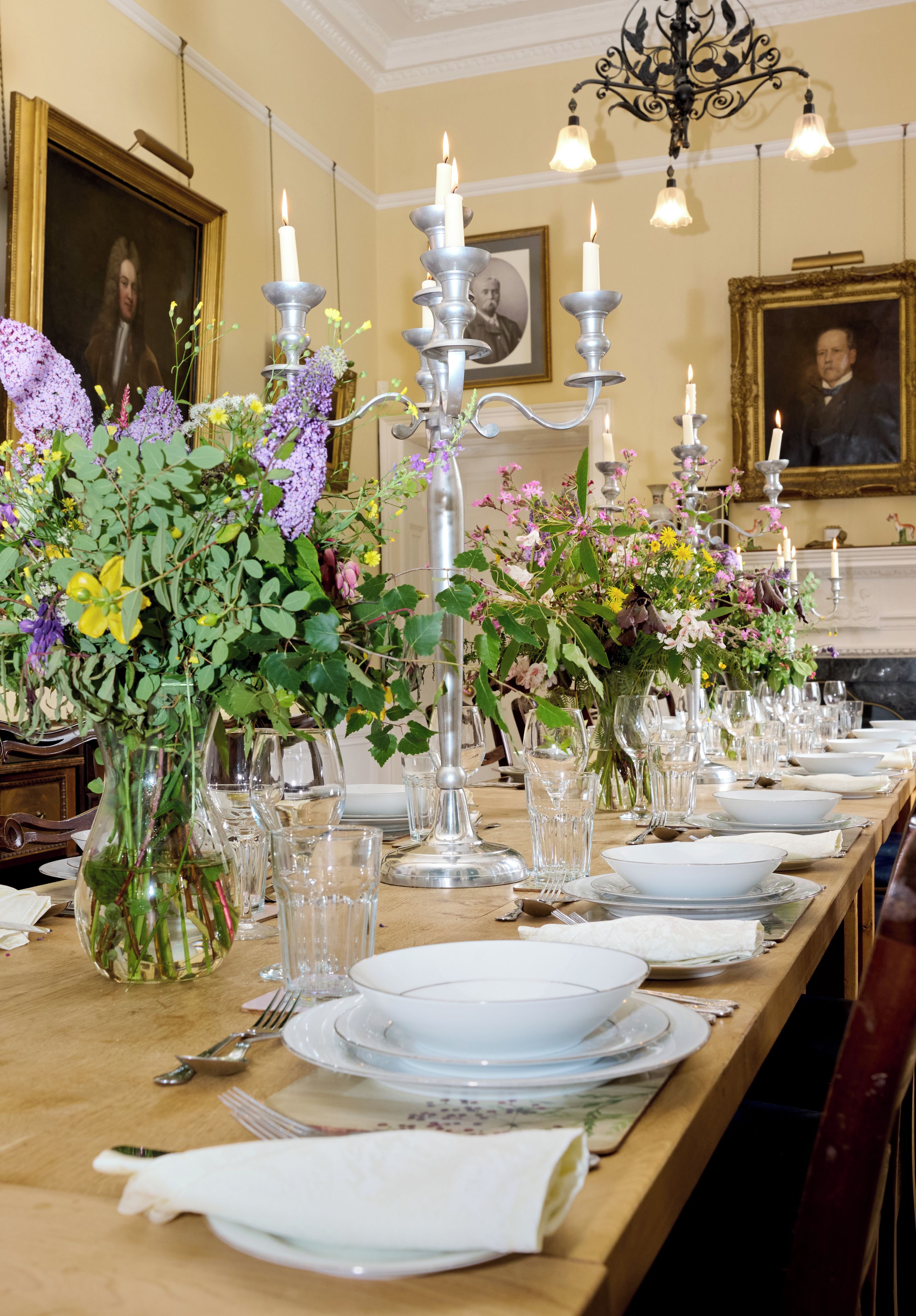 A formal dining table set with glassware, plates, and silverware, flanked by floral arrangements and candelabras.
