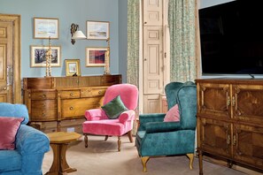 A room with a wooden cabinet, a pink armchair, a teal armchair, and a blue sofa.