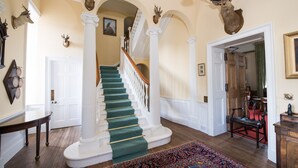 A grand staircase with a green carpet, white columns, and deer heads on the walls. - Classically beautiful large family friendly retreat, situated on the Moray Firth (Moray)