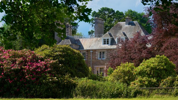 A large stone house with multiple chimneys, surrounded by lush greenery and flowering bushes. - Classically beautiful large family friendly retreat, situated on the Moray Firth (Moray)
