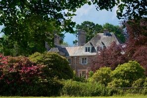 A large stone house with multiple chimneys, surrounded by lush greenery and flowering bushes. - Classically beautiful large family friendly retreat, situated on the Moray Firth (Moray)