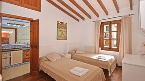 Una habitación con dos camas, vigas de madera en el techo, una ventana con cortinas, un radiador y un espejo con detalles de azulejos.