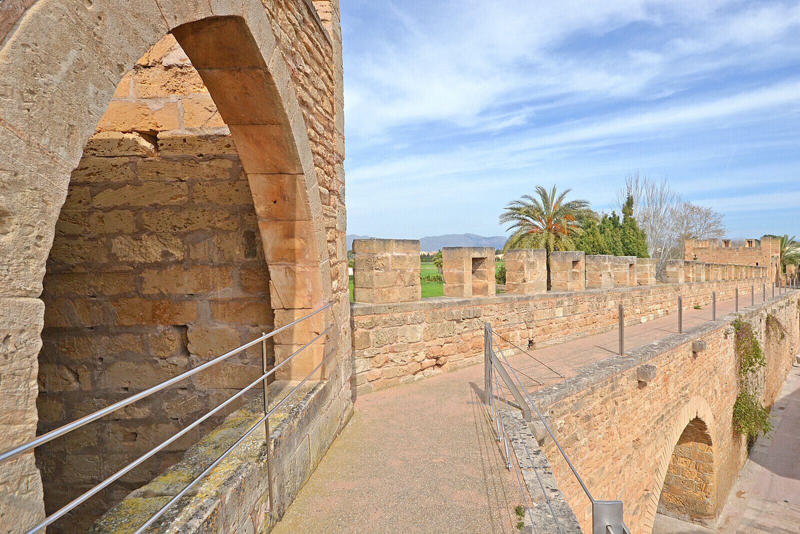 A stone bridge with an archway, a pathway, and a view of the surrounding landscape including trees and a distant mountain.