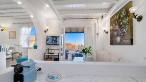 A spacious living area with a large window offering a scenic view, a television mounted on the wall, and a seating area with a sofa and a coffee table.