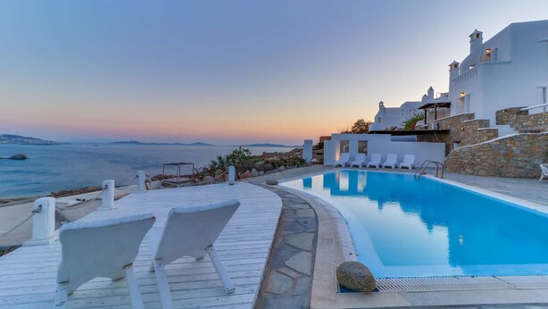 A pool area with a view of the sea and a white building with stone accents.