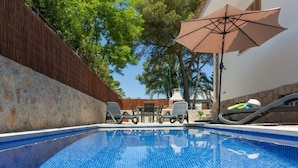 A swimming pool with tiled blue floor, surrounded by lounge chairs and a table, with a wooden fence and trees in the background. - Marblava - Cosy villa with swimming pool 100 m from the beach (Muro (Platja de Muro))