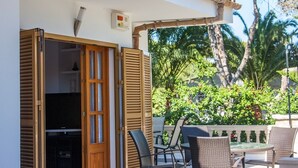 An outdoor patio with a table and chairs, a wooden door, and a view of greenery and trees. - Marblava - Cosy villa with swimming pool 100 m from the beach (Muro (Platja de Muro))