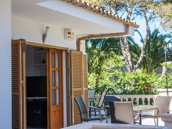 An outdoor patio with a table and chairs, a wooden door, and a view of greenery and trees.