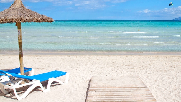 A beach with clear turquoise water, a wooden walkway, and blue lounge chairs under a thatched umbrella. - Marblava - Cosy villa with swimming pool 100 m from the beach (Muro (Platja de Muro))