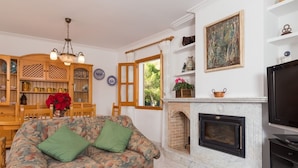 A living room with a sofa, a fireplace, a television, and a dining area with a wooden cabinet and table. - Marblava - Cosy villa with swimming pool 100 m from the beach (Muro (Platja de Muro))