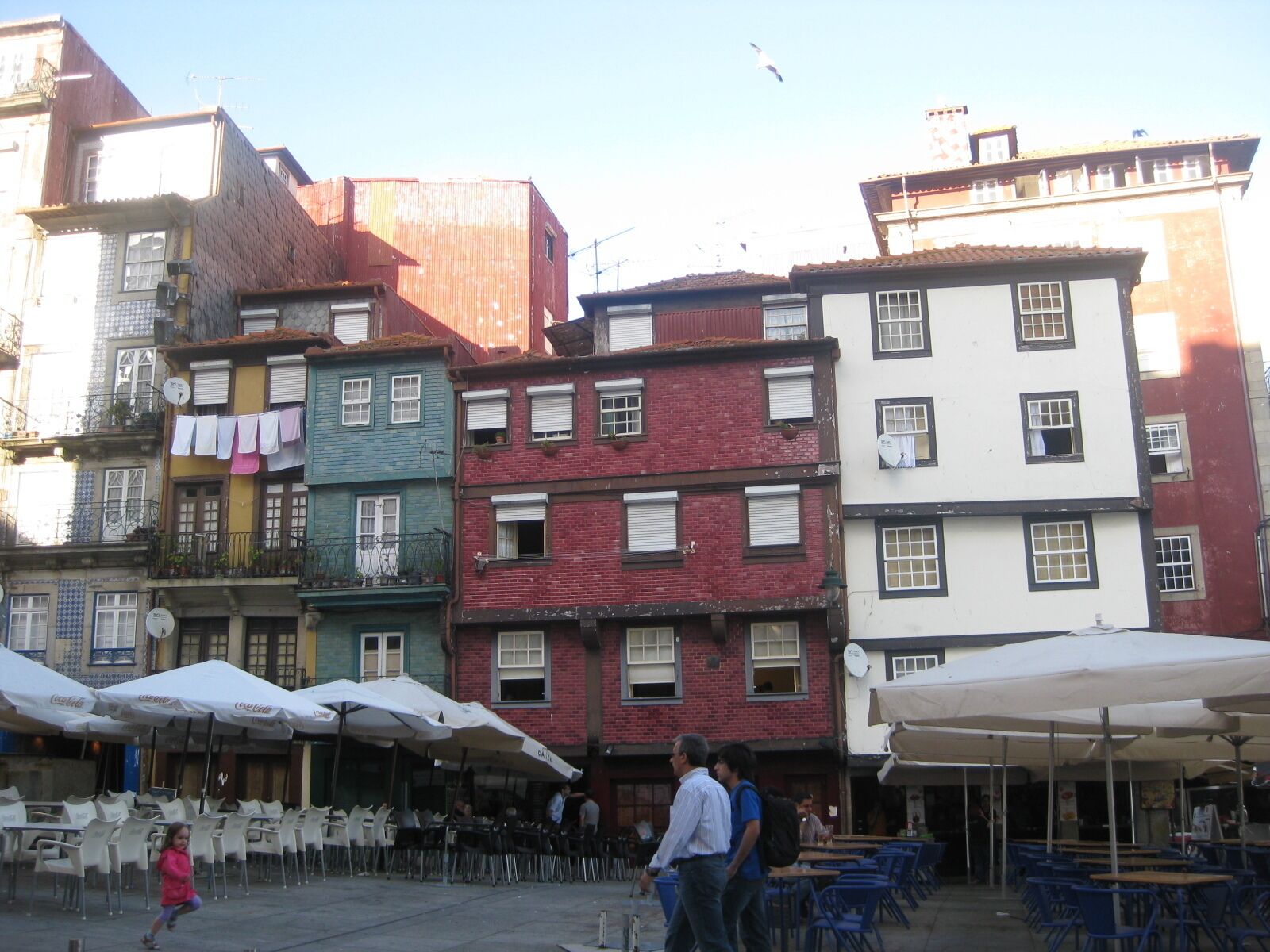 Une rue bordée de bâtiments aux couleurs vives, avec des terrasses et des passants.