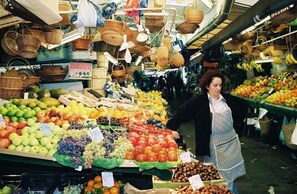 A market stall with various fruits and vegetables on display, including apples, grapes, and tomatoes.