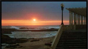 A sunset view from a balcony overlooking a rocky beach with waves crashing onto the shore.