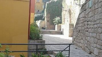 Une ruelle étroite pavée, bordée de plantes en pot et d’un mur de pierre.