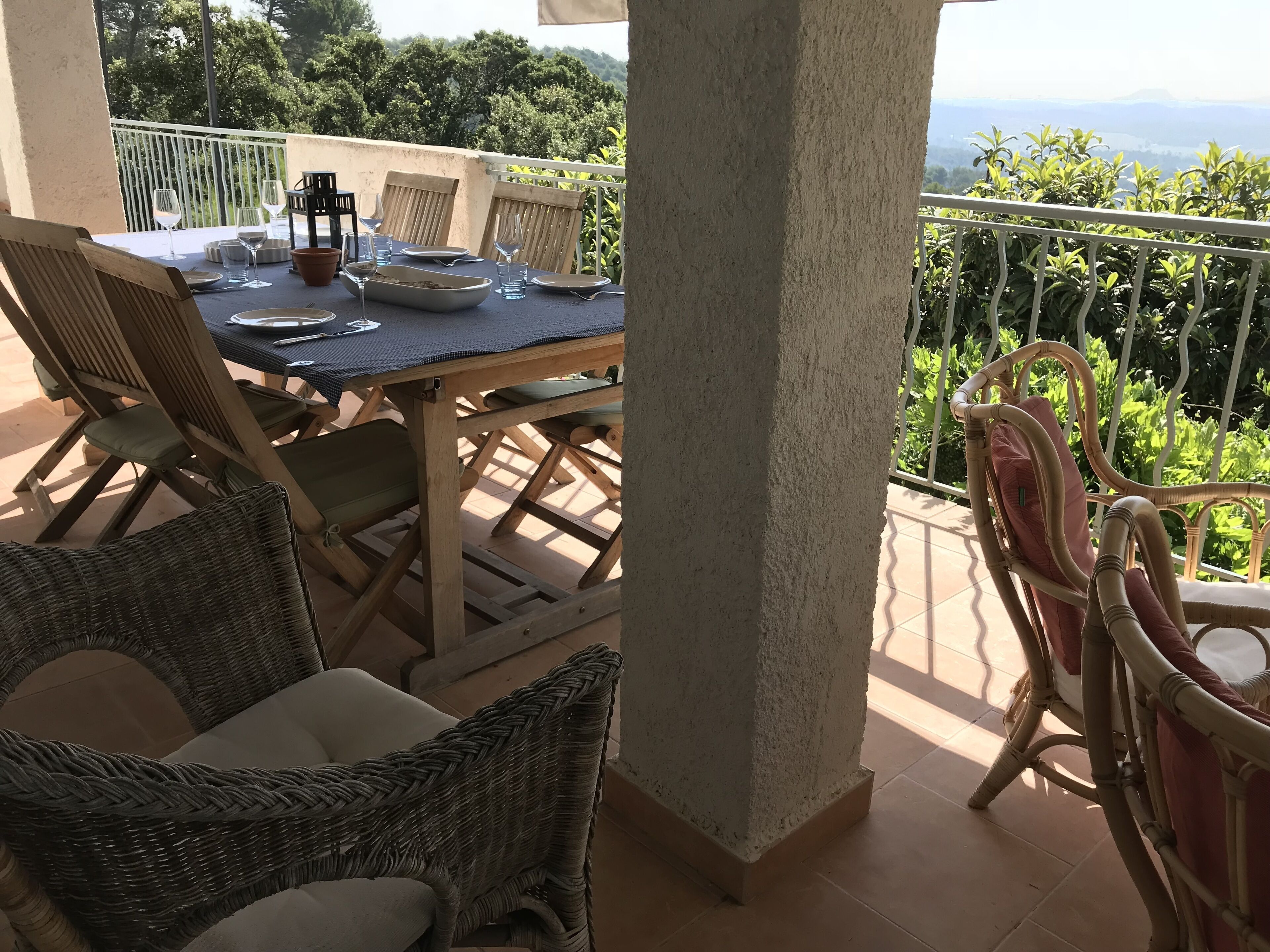Una terraza con mesa lista para comer, sillas de mimbre y vistas a zonas verdes y colinas.