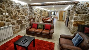 Un salon avec un mur en pierre, un canapé en cuir marron, un tapis rouge et un coin repas à l’arrière-plan.