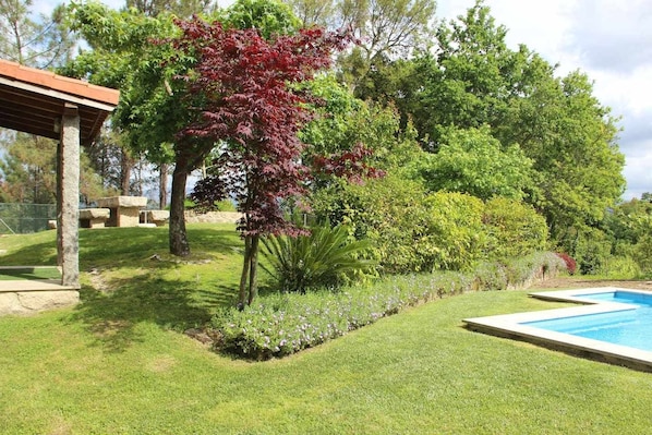 A well-maintained garden with a swimming pool, stone structures, and a variety of trees and shrubs.