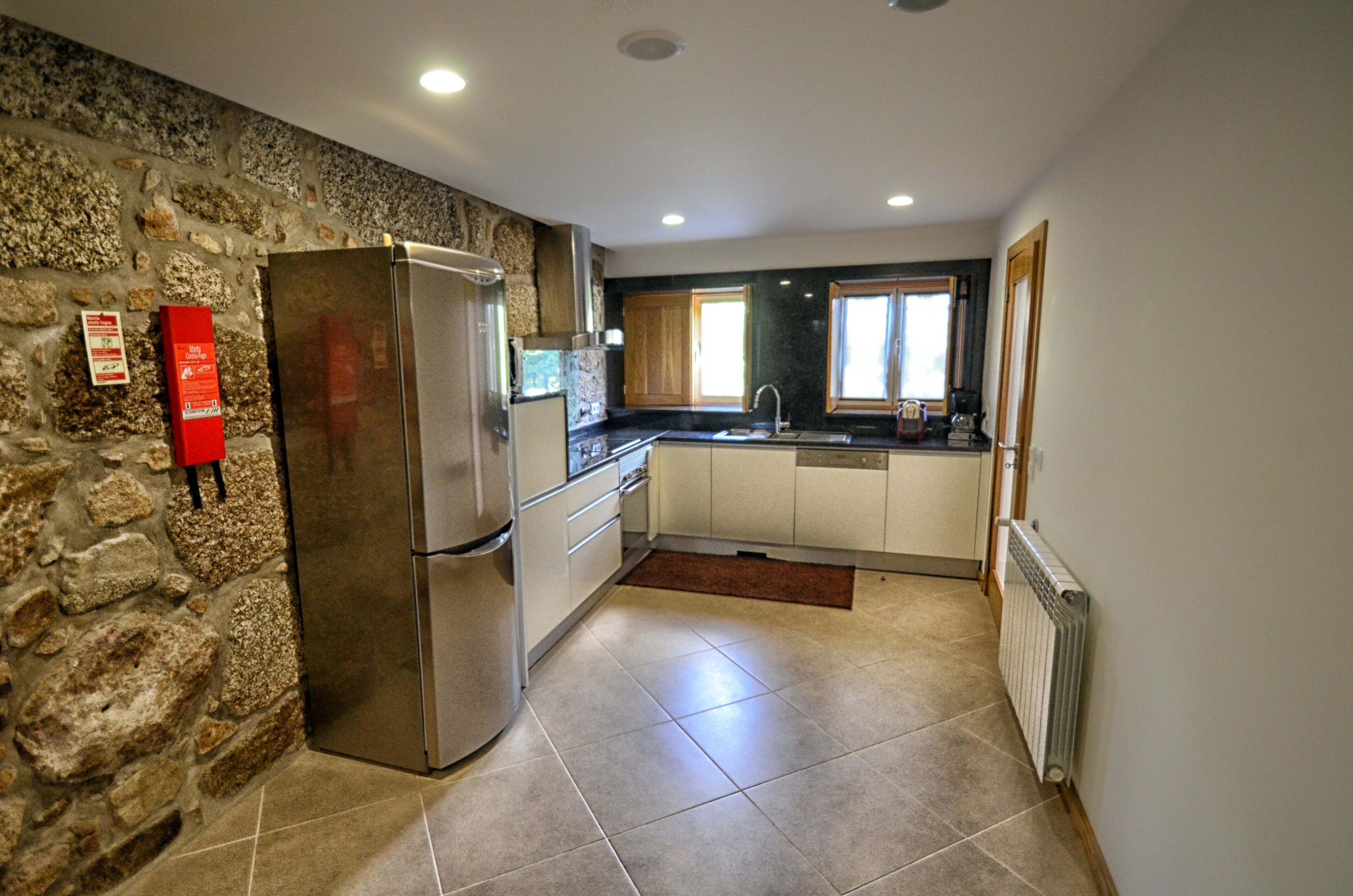 A kitchen with a stone wall, a refrigerator, cabinets, a sink, and a window.