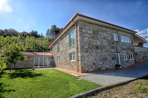 A stone building with a tiled roof, a covered patio, and a grassy yard.