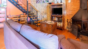 A cozy living room with a wooden staircase, a stone wall, a fireplace, and a television. - Romantic Escape with Terrace (La Omañuela, León)