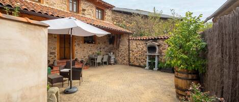 A stone building with a tiled roof, outdoor seating, and a brick patio.