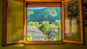 A window with a view of a forested hillside and a balcony with potted plants. - Romantic Escape with Terrace (La Omañuela, León)