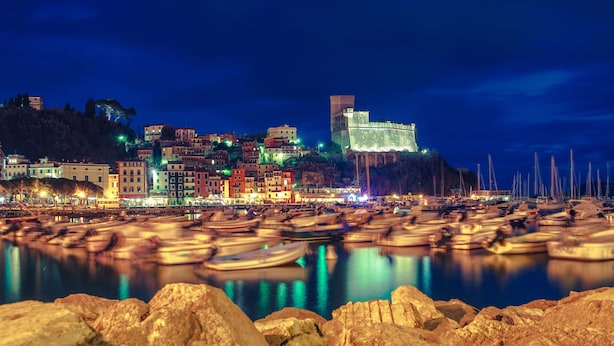 A coastal town at night with illuminated buildings, a prominent castle-like structure, and numerous boats docked along the shore. - Luxury Private Villa with 15mx6m Pool. Private Setting with Panoramic views (orturano, bagnone)