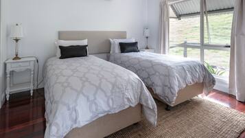 A bedroom with two beds, a window with curtains, a bedside table with a lamp, and a wall-mounted air conditioner.