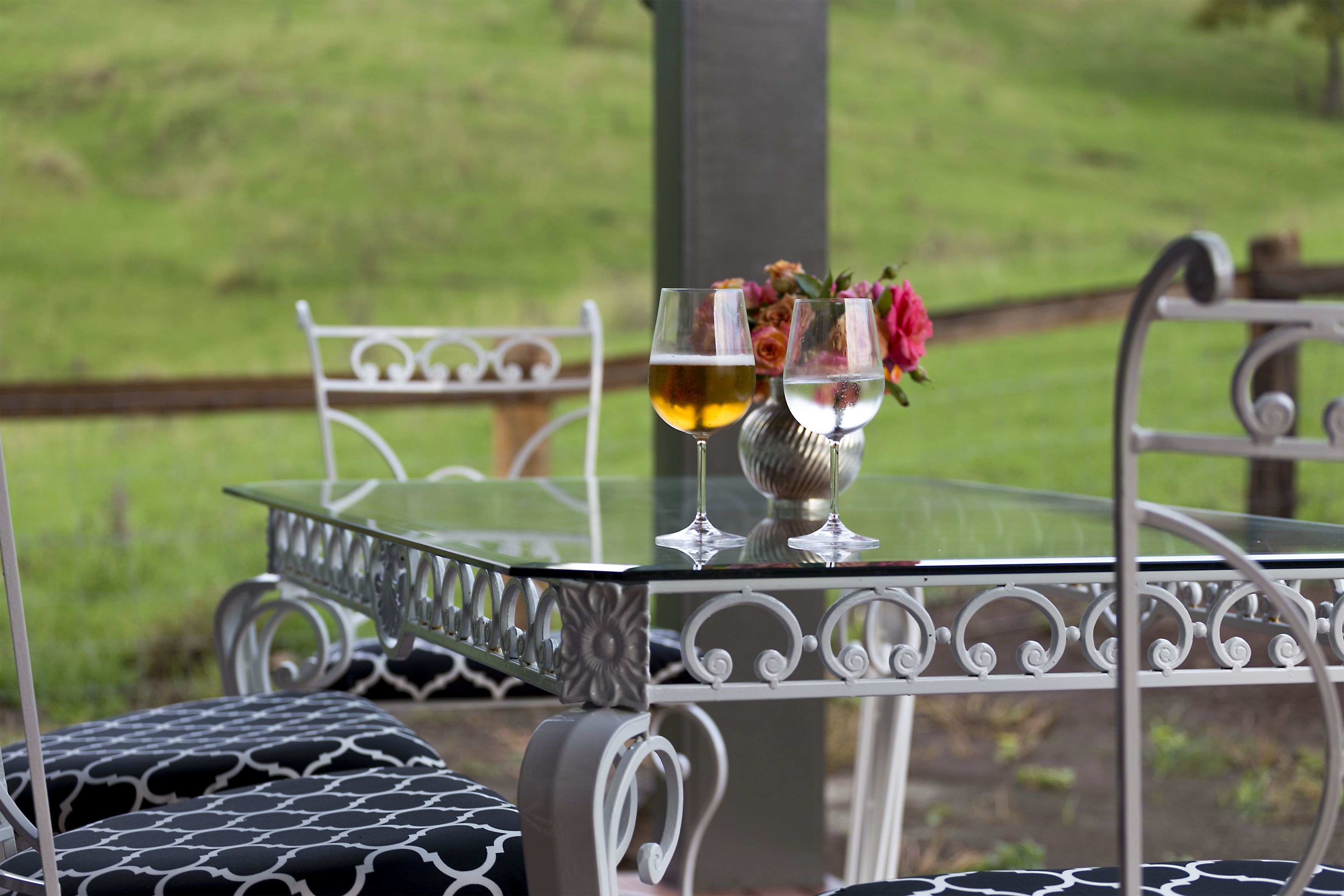 Una mesa de cristal con dos copas de vino y un jarrón con flores.