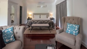 A hotel room with a bed, two armchairs, a coffee table, and a bedside table with lamps. - Country Mile Escape (Flying Fox)