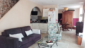 A living room with a sofa, a glass coffee table, and a patterned armchair. There is a kitchen area with cabinets and a refrigerator. - In the heart of Provence, near the verdon stone house of character (Varages)