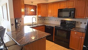 Una cocina con armarios de madera, encimera de granito, horno microondas integrado, estufa y pileta.