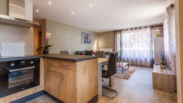 Een moderne keuken met een centraal eiland, een ingebouwde oven en een eethoek met een tafel en stoelen.