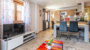 Een moderne woonkamer met een televisie, zithoek en een kleine keuken.