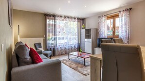 Een moderne woonkamer met een bank, fauteuil en salontafel. Achterin staat een televisie en een koelkast.