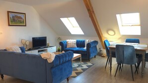 Un apartamento estilo loft acogedor con comedor, dos sofás azules, un televisor y un cuadro en la pared.