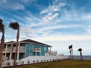 A two-story house with a white fence, a balcony, and a view of the ocean.
