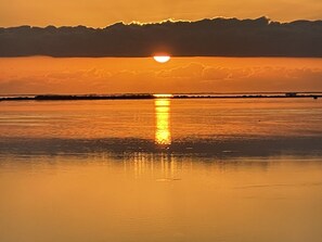 A sunset over a calm body of water with a bridge in the distance.
