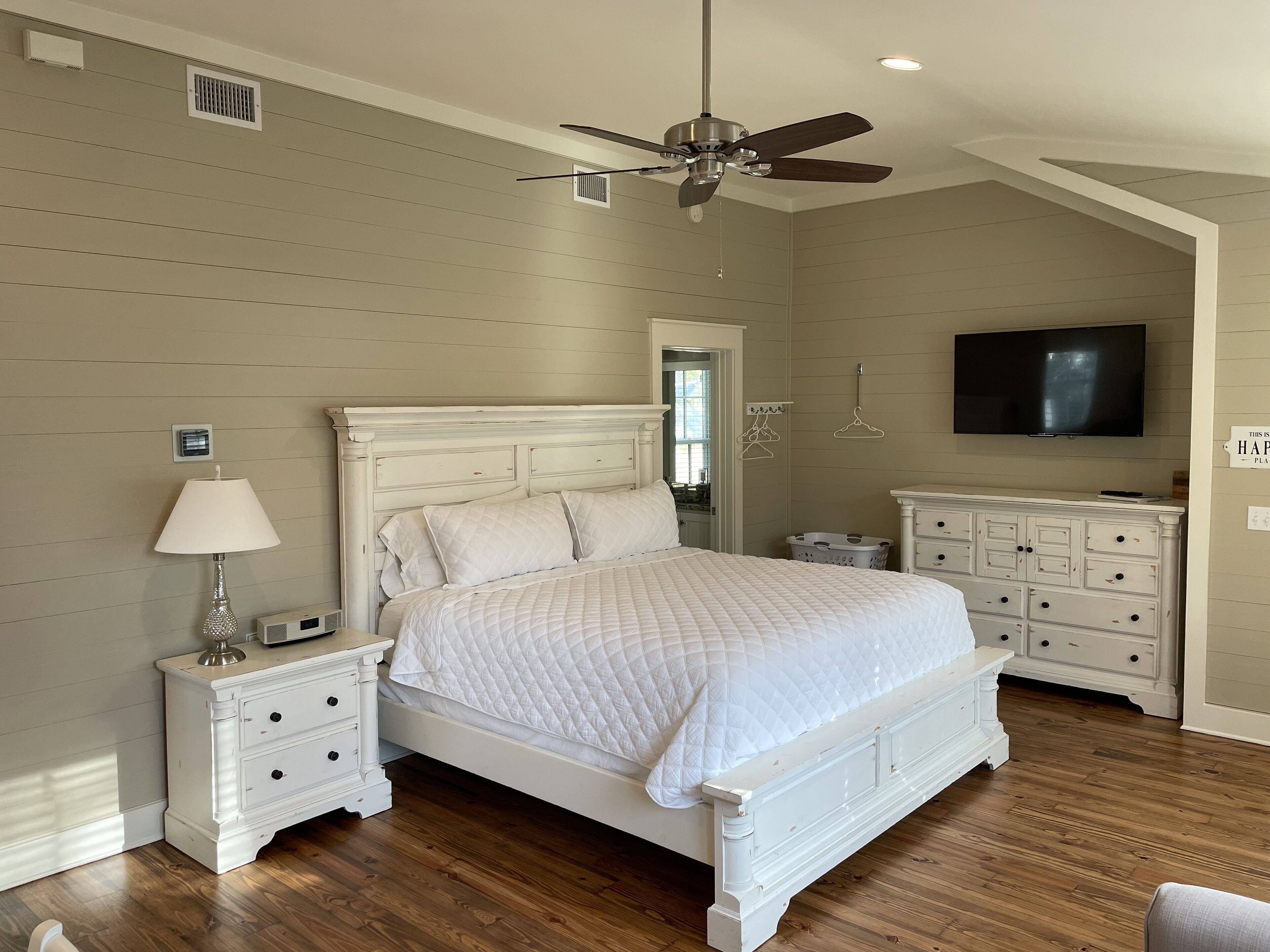 Une chambre à coucher comprenant un lit, des tables de chevet, une lampe, un ventilateur de plafond, un téléviseur et une commode.