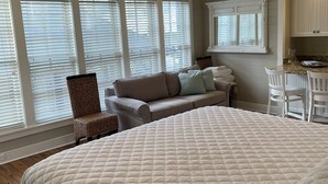 A bedroom with a large bed, a ceiling fan, a window with blinds, a sofa, and a small table. - Steps away from Camp Watercolor Amenities  (Santa Rosa Beach)