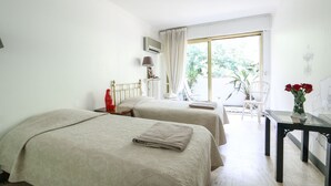 Habitación de hotel con dos camas, una mesita con un florero y una silla, y vistas al exterior.
