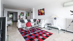 Una sala de estar moderna con un sofá blanco, una mesa de centro de vidrio y un tapete colorido a cuadros.