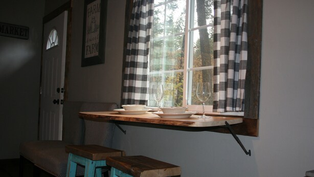 A kitchen with a window, a wooden table, and two stools. - Tiny Red Farmhouse centrally located in Columbia Falls (Columbia Falls)