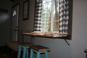 Een keuken met een raam, een houten tafel en twee krukken.