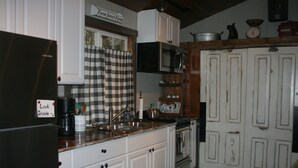 A kitchen with white cabinets, a black refrigerator, a microwave, and a stove. There is a sign above the window that reads "Farm Sweet Farm." - Tiny Red Farmhouse centrally located in Columbia Falls (Columbia Falls)
