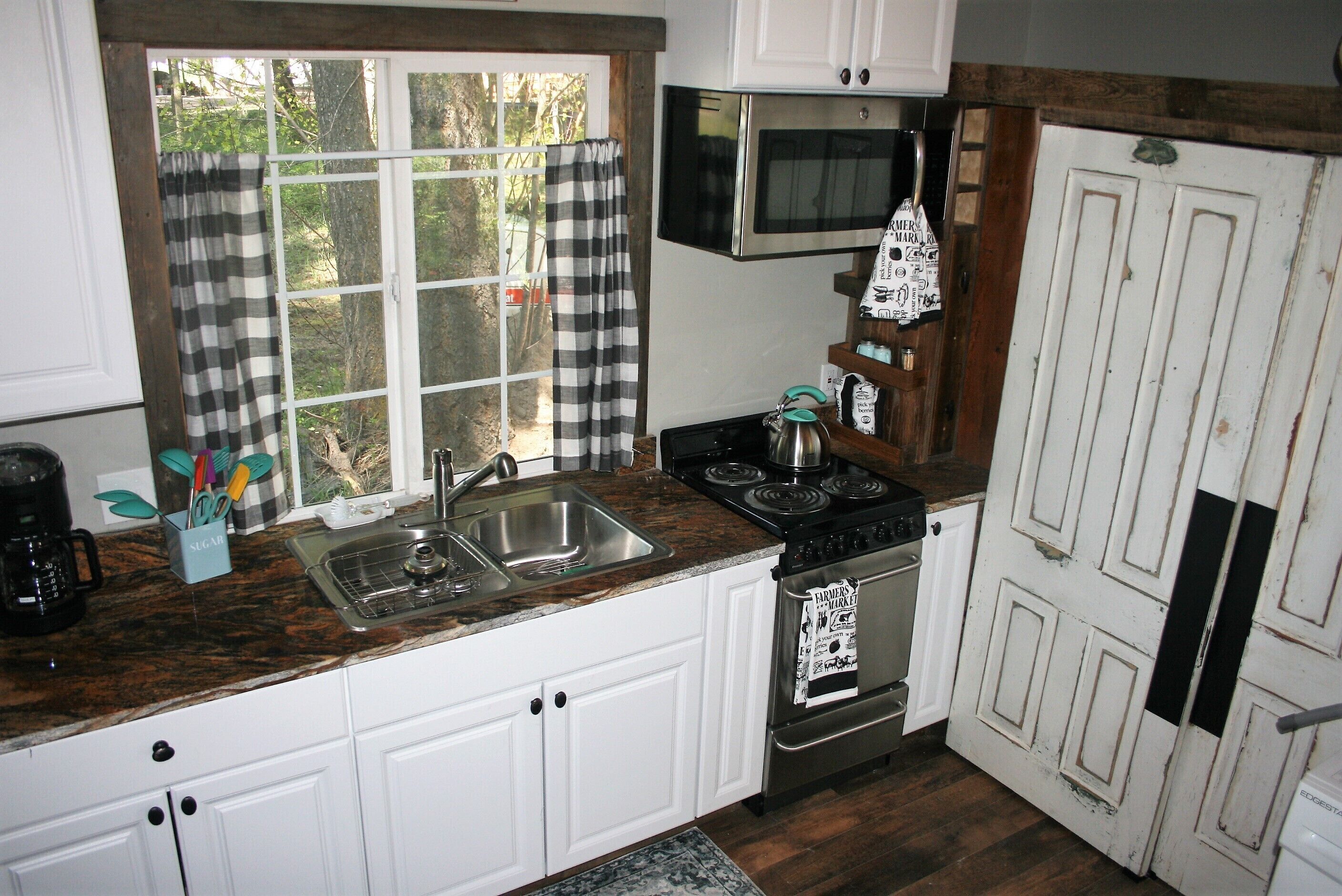 A kitchen with white cabinets, a stainless steel microwave, a stove, and a sink.