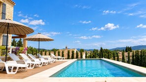 Una piscina con sillas de descanso y sombrillas, rodeada de un muro de piedra y árboles.